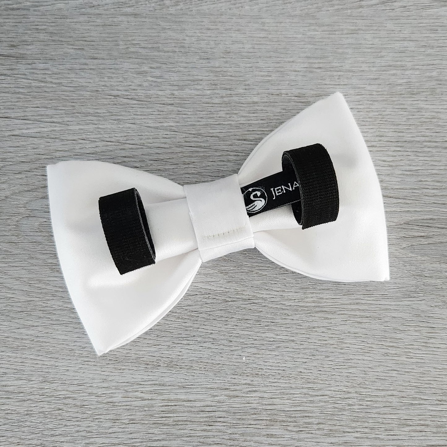 A white dog bow tie in matte satin fabric with Velcro tapes to attach to the collar.