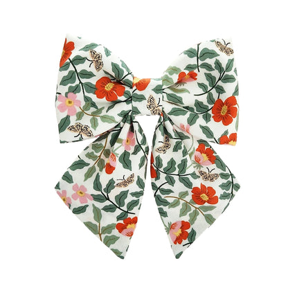 A dog bow for the collar in an orange and pink flower print with vines and butterflies.