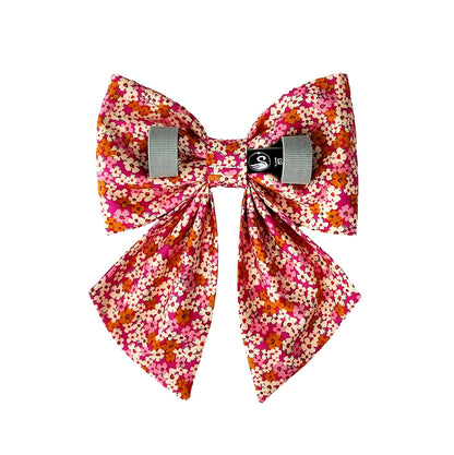 A back view of a dog sailor bow with mini floral print on a hot pink background. Velcro tapes on the back attach it to the collar.